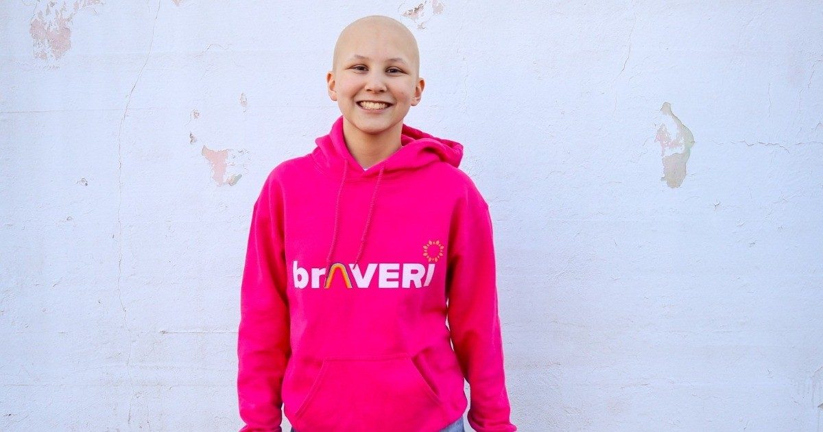 Averi Brown standing in front of a white wall wearing a pink sweatshirt with the words "braveri" on it.